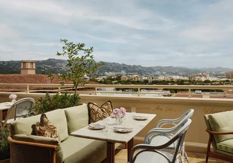 Al fresco lounge on the rooftop at Dante Beverly Hills with marble tables, green cushions, and city skyline views above “Where Dreams Are Made.”