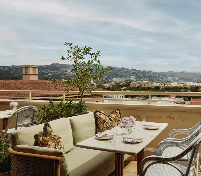 Al fresco lounge on the rooftop at Dante Beverly Hills with marble tables, green cushions, and city skyline views above “Where Dreams Are Made.”
