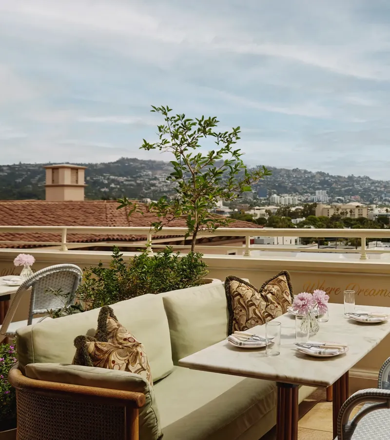 Al fresco lounge on the rooftop at Dante Beverly Hills with marble tables, green cushions, and city skyline views above “Where Dreams Are Made.”