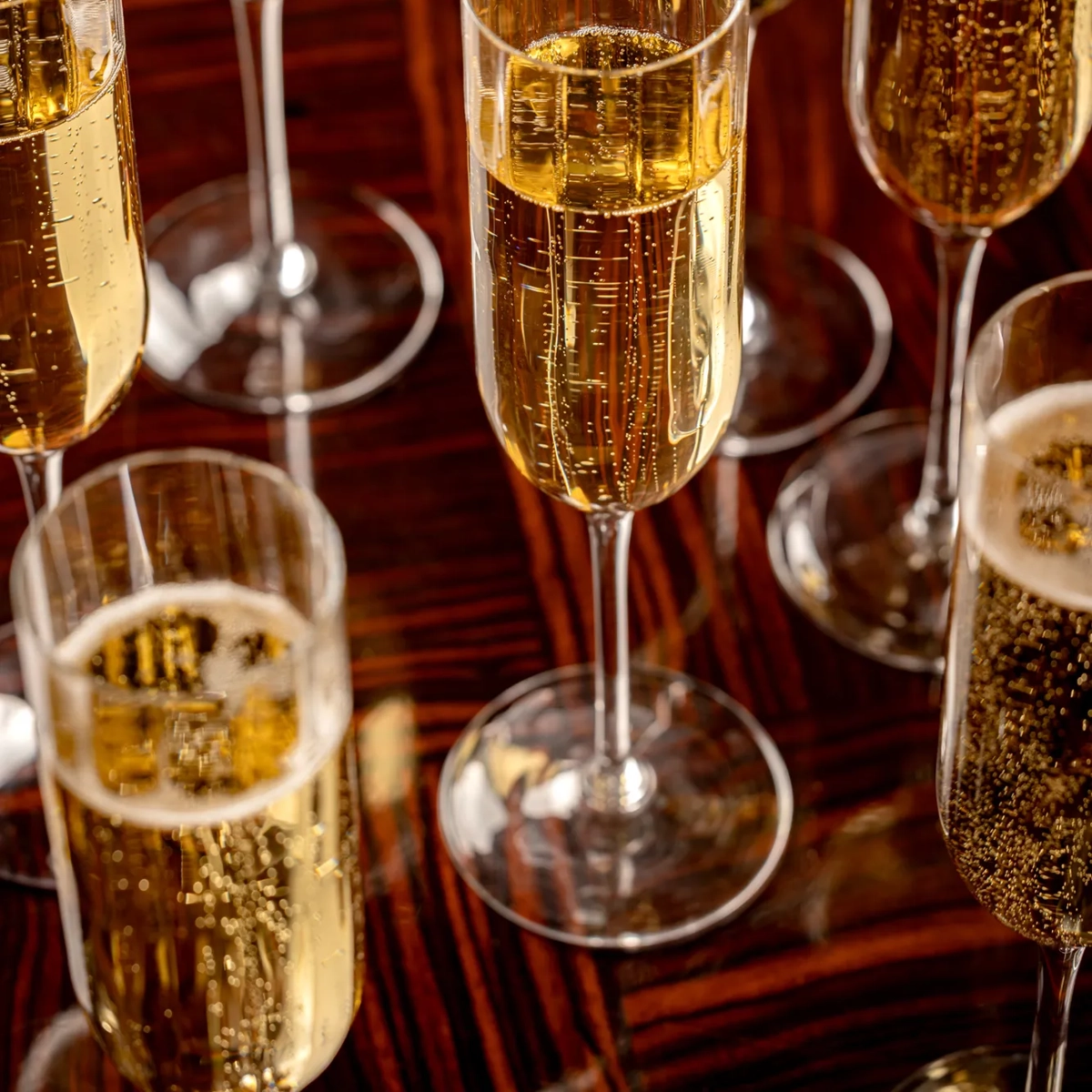 Close-up of champagne flutes filled with sparkling wine on a polished wooden table.
