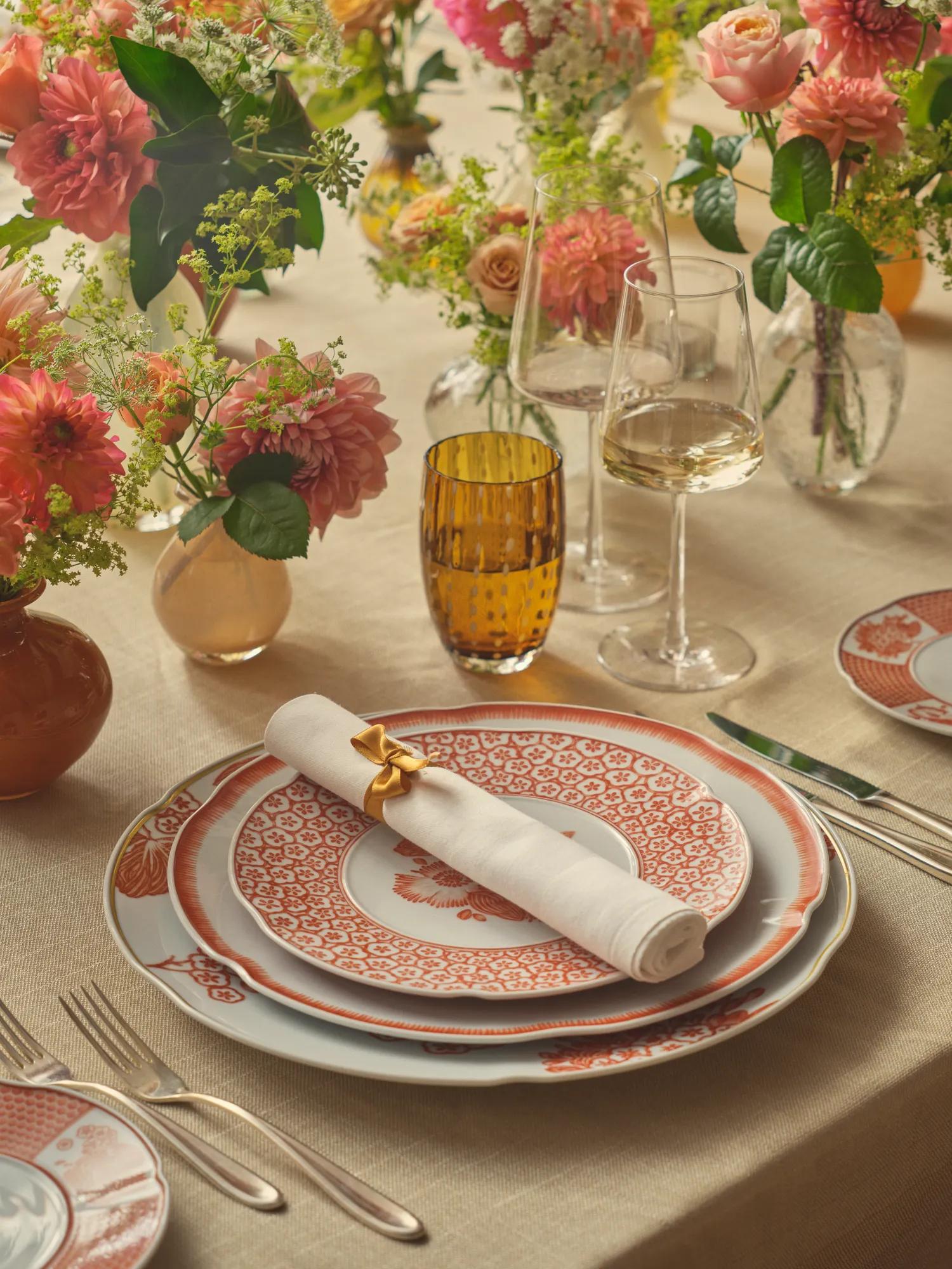 Elegant table set with floral arrangements, wine glasses, and fine china with red and white patterns.