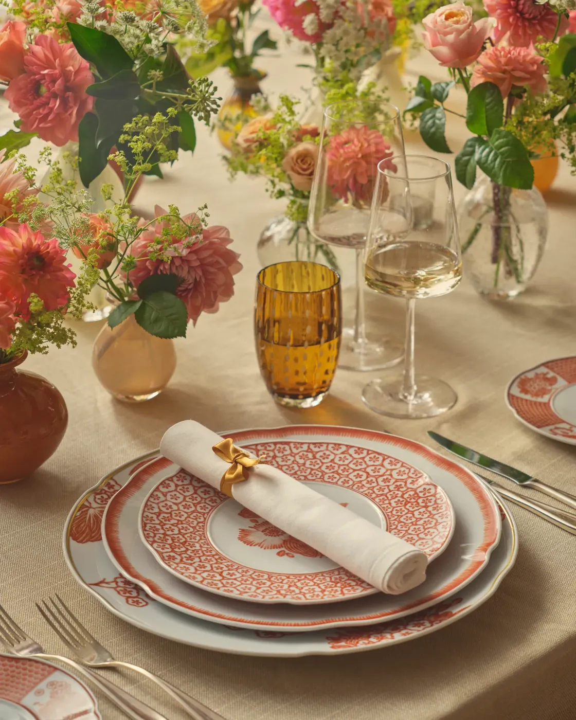 Elegant table set with floral arrangements, wine glasses, and fine china with red and white patterns.