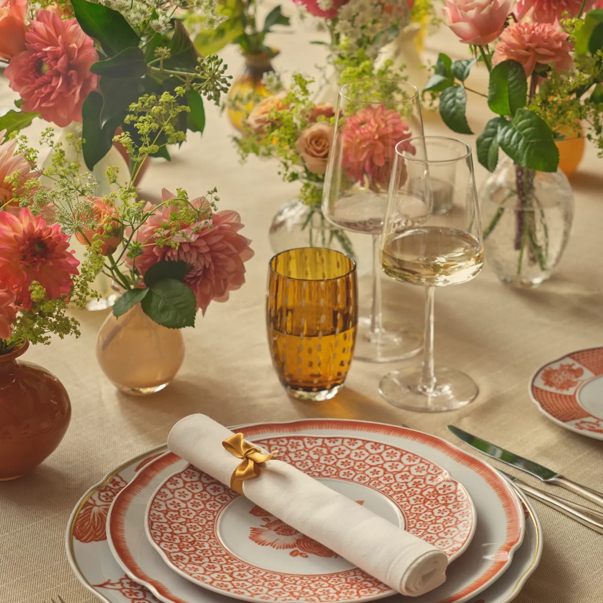 Elegant table set with floral arrangements, wine glasses, and fine china with red and white patterns.