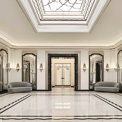 The Ballroom reception area at Claridge’s featuring polished marble floors, mirrored Art Deco wall panels, grey velvet sofas, and a large geometric skylight ceiling.
