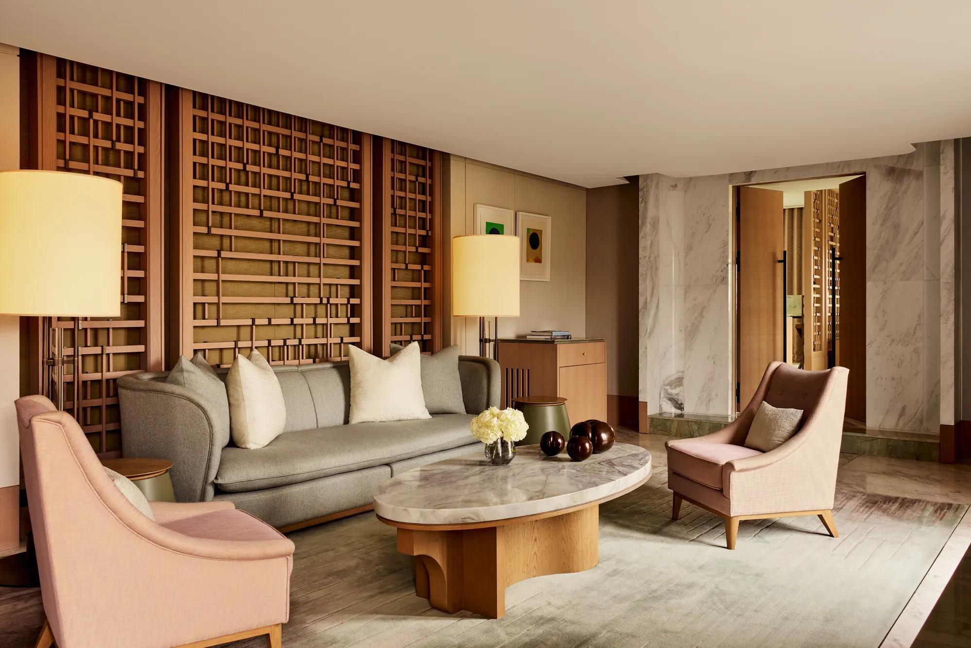 Elegant sitting area with marble coffee table, grey sofa, pink armchairs, and wooden lattice wall panels