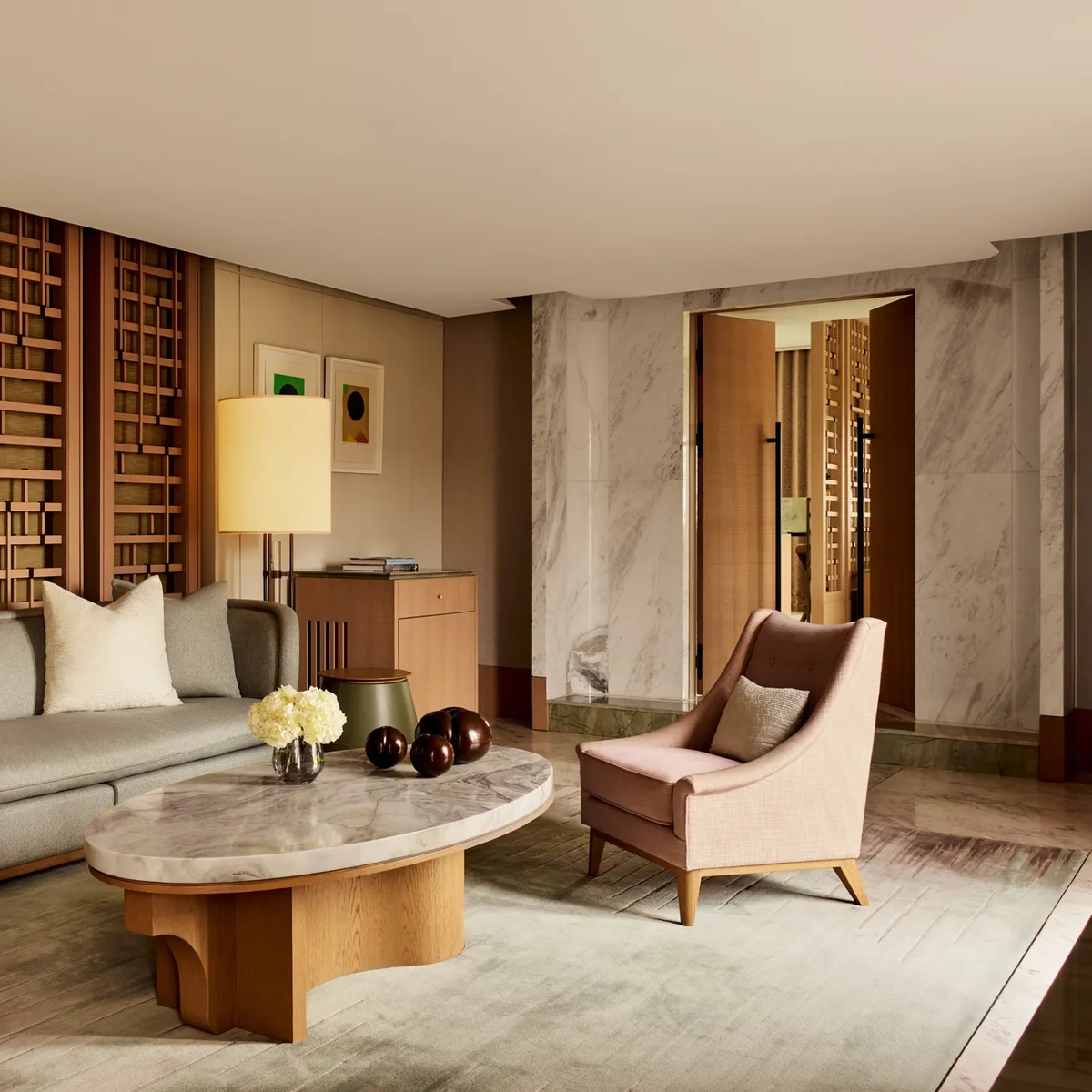 Elegant sitting area with marble coffee table, grey sofa, pink armchairs, and wooden lattice wall panels