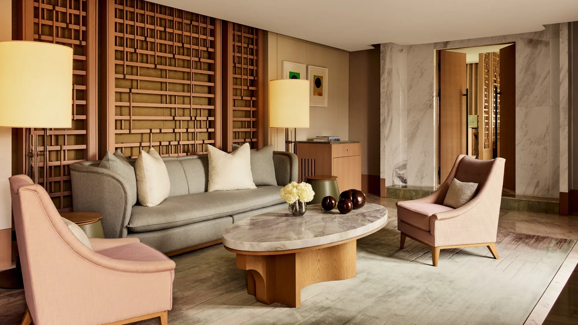 Elegant sitting area with marble coffee table, grey sofa, pink armchairs, and wooden lattice wall panels