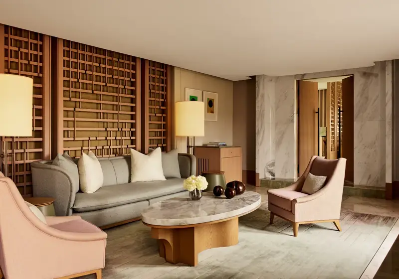 Elegant sitting area with marble coffee table, grey sofa, pink armchairs, and wooden lattice wall panels