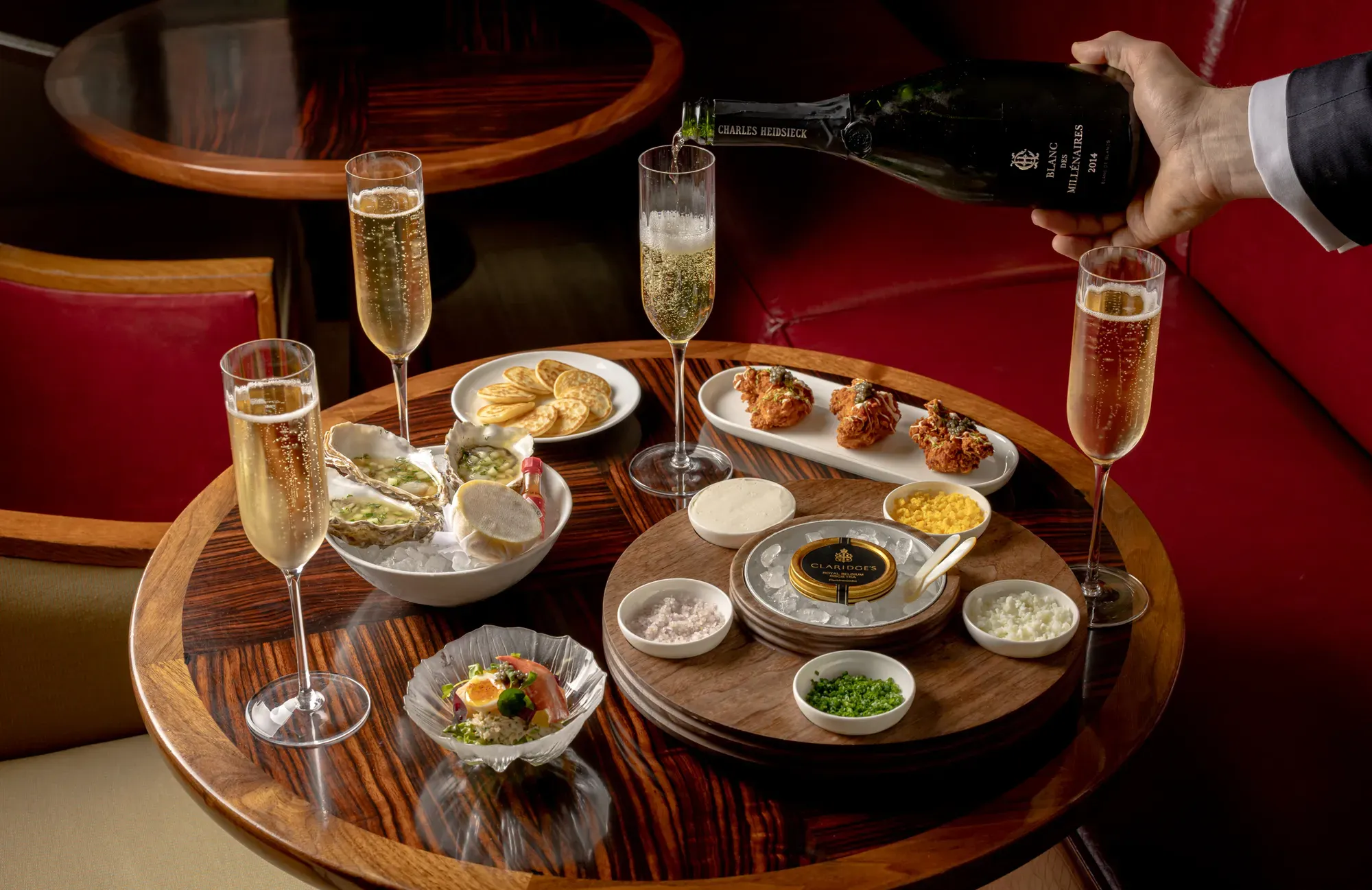 Champagne poured over caviar, oysters, and canapés on a polished table in a red leather booth setting
