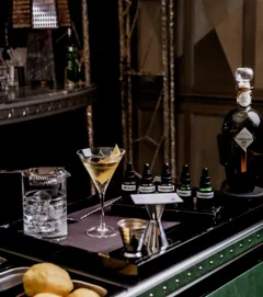 Martini trolley with mixing tools, citrus, bitters bottles, and a prepared martini beside a Connaught Bar gin bottle.