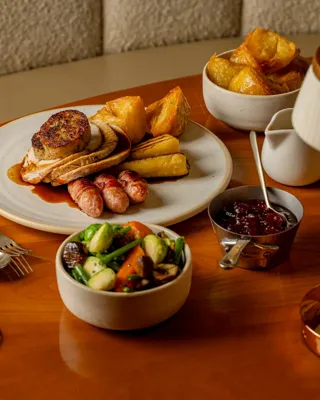 Roast dinner with turkey, stuffing, sausages, potatoes, vegetables, gravy and a glass of sparkling wine on a table.