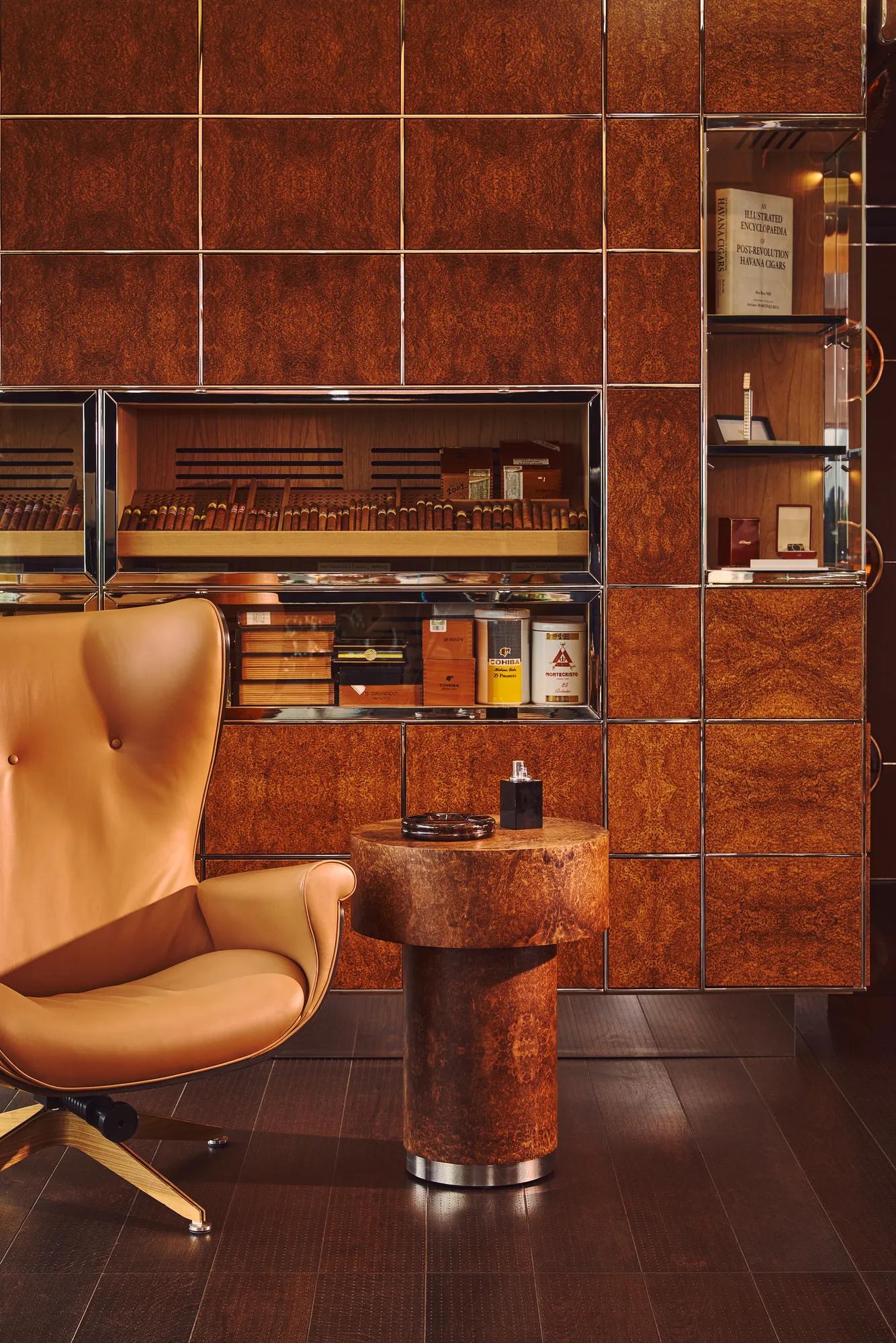 A tan leather armchair beside a round wooden table in a cigar lounge with wood-panelled walls and display cabinets.