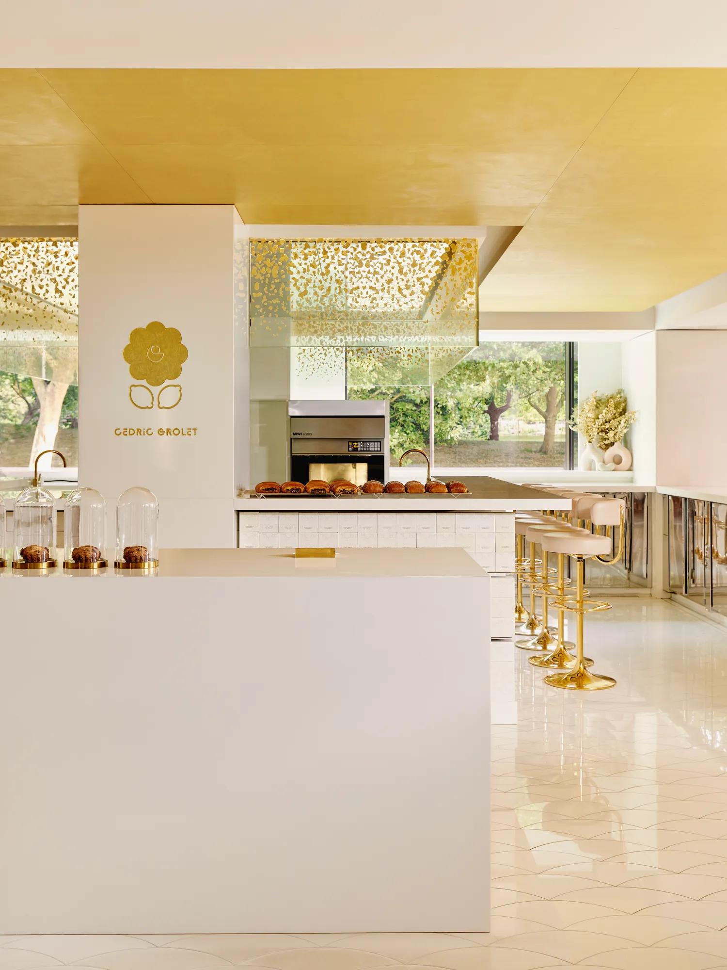 Bright patisserie interior with gold accents, marble counter, and pastries displayed beneath glass cloches.