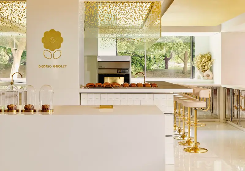 Bright patisserie interior with gold accents, marble counter, and pastries displayed beneath glass cloches.