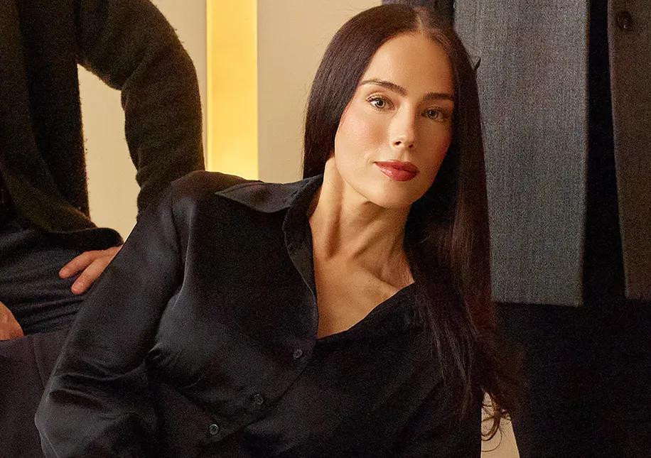 Portrait of a woman in a black blouse with long dark hair, seated indoors in warm lighting