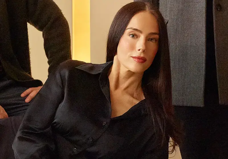Portrait of a woman in a black blouse with long dark hair, seated indoors in warm lighting