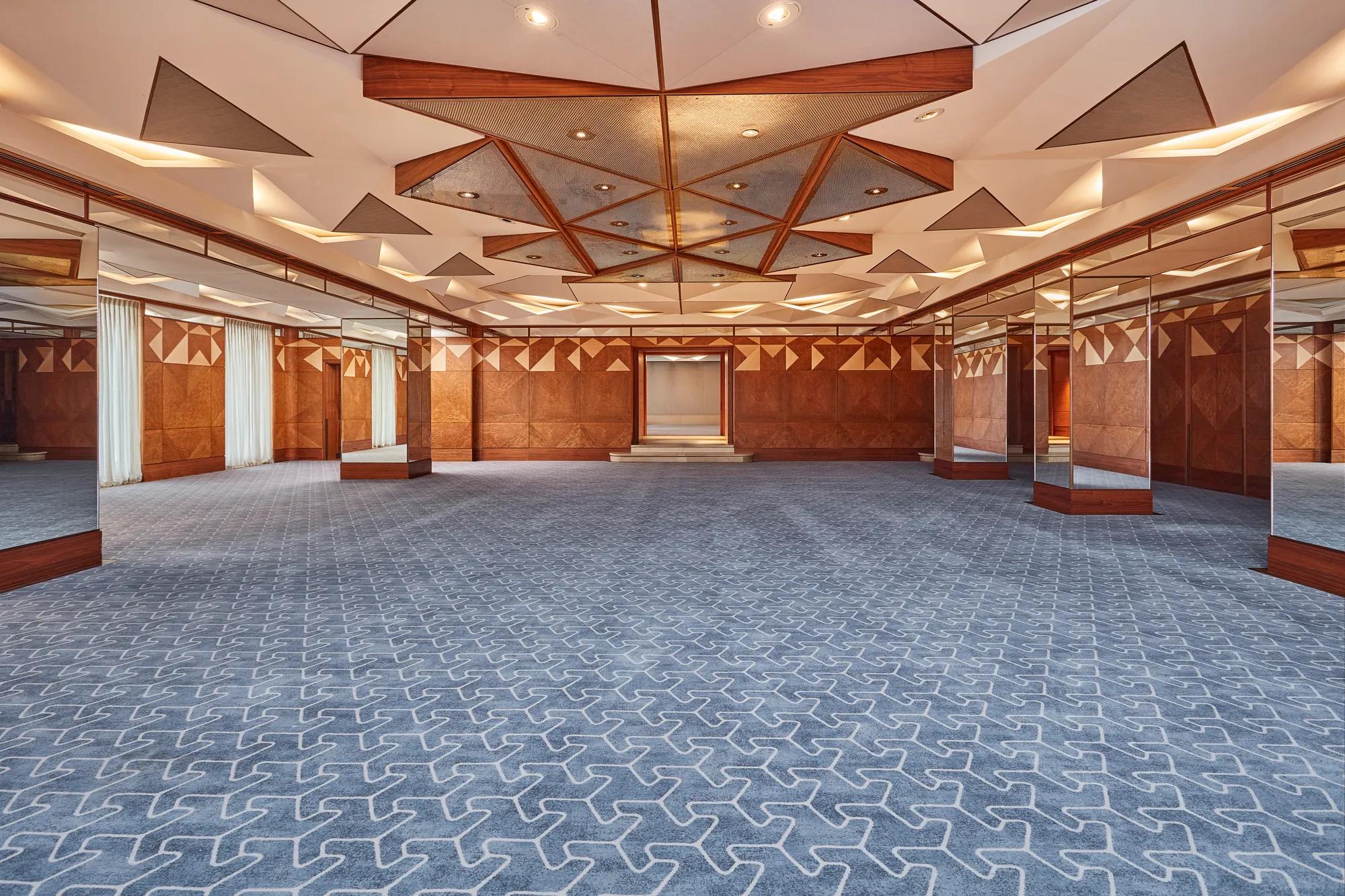 Spacious hotel ballroom with geometric ceiling design, patterned carpet, and mirrored walls for events