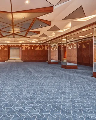 Spacious hotel ballroom with geometric ceiling design, patterned carpet, and mirrored walls for events