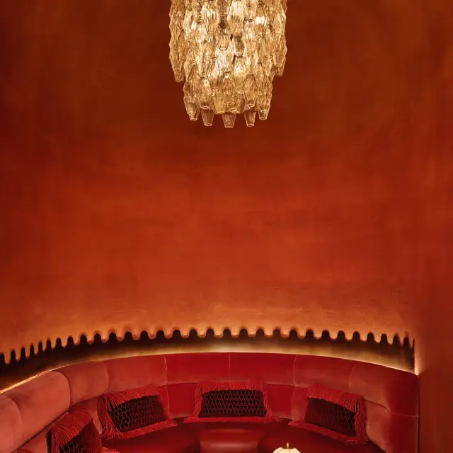 Intimate red alcove with curved velvet seating, a sculpted marble table, and a crystal chandelier overhead.