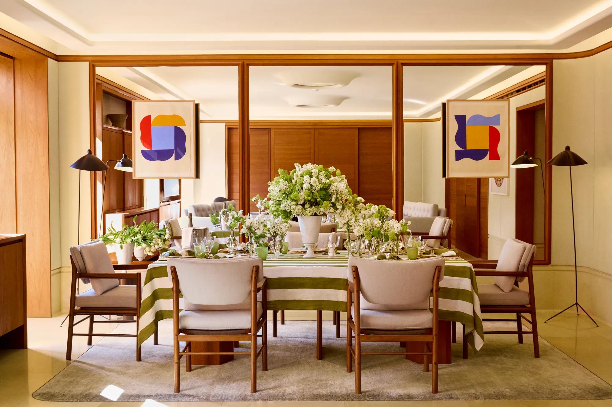 Elegant dining room with a long table dressed in striped linens, white floral arrangements and upholstered chairs, framed by mirrored panels and modern artwork.