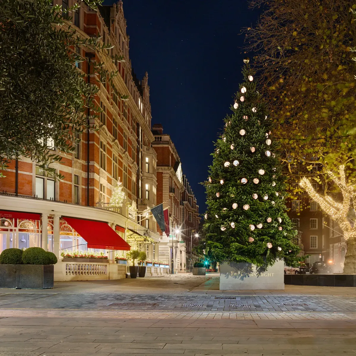 Decorated Christmas tree with round ornaments outside The Connaught on a quiet Mayfair night.