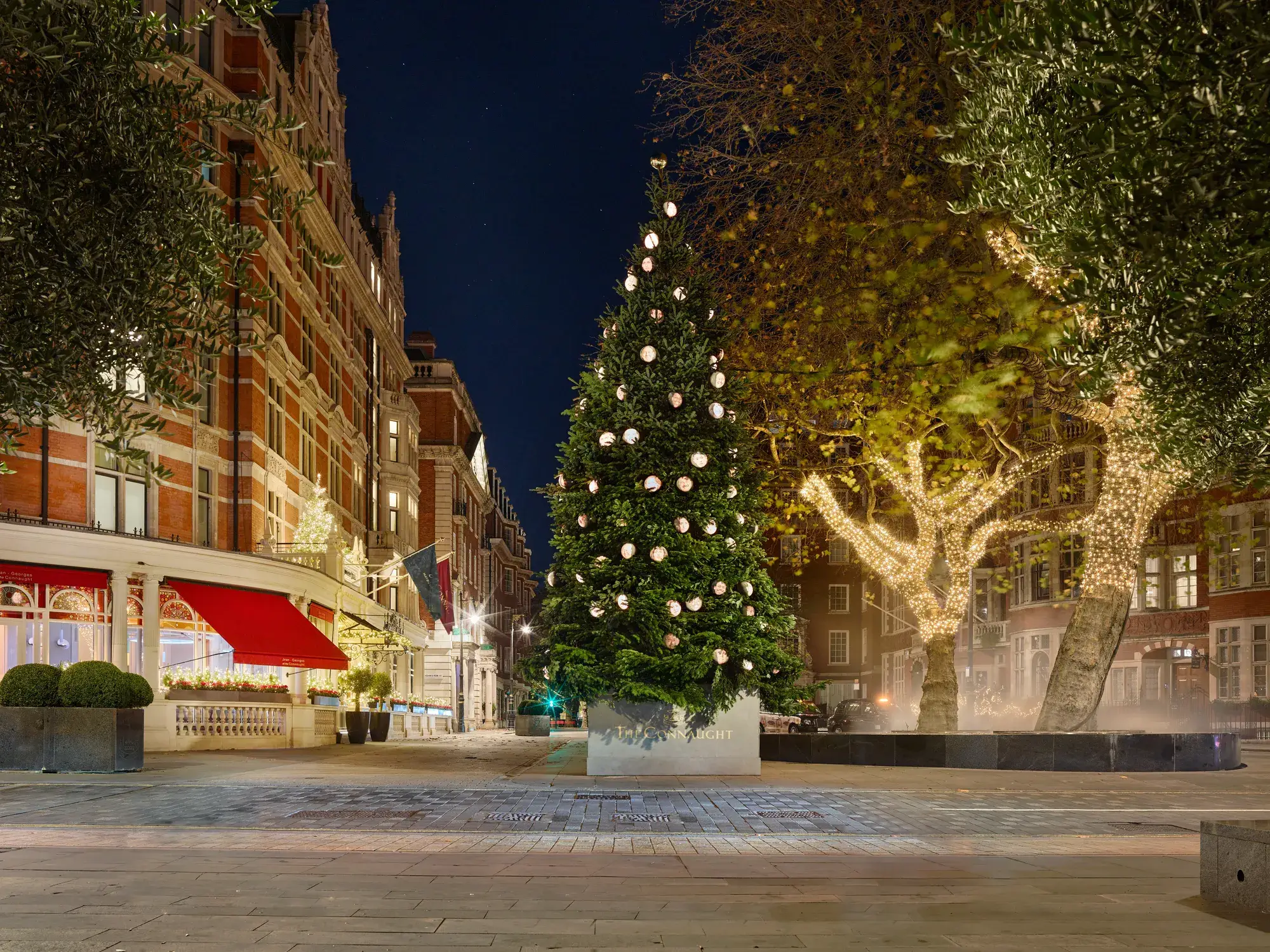 Decorated Christmas tree with round ornaments outside The Connaught on a quiet Mayfair night.