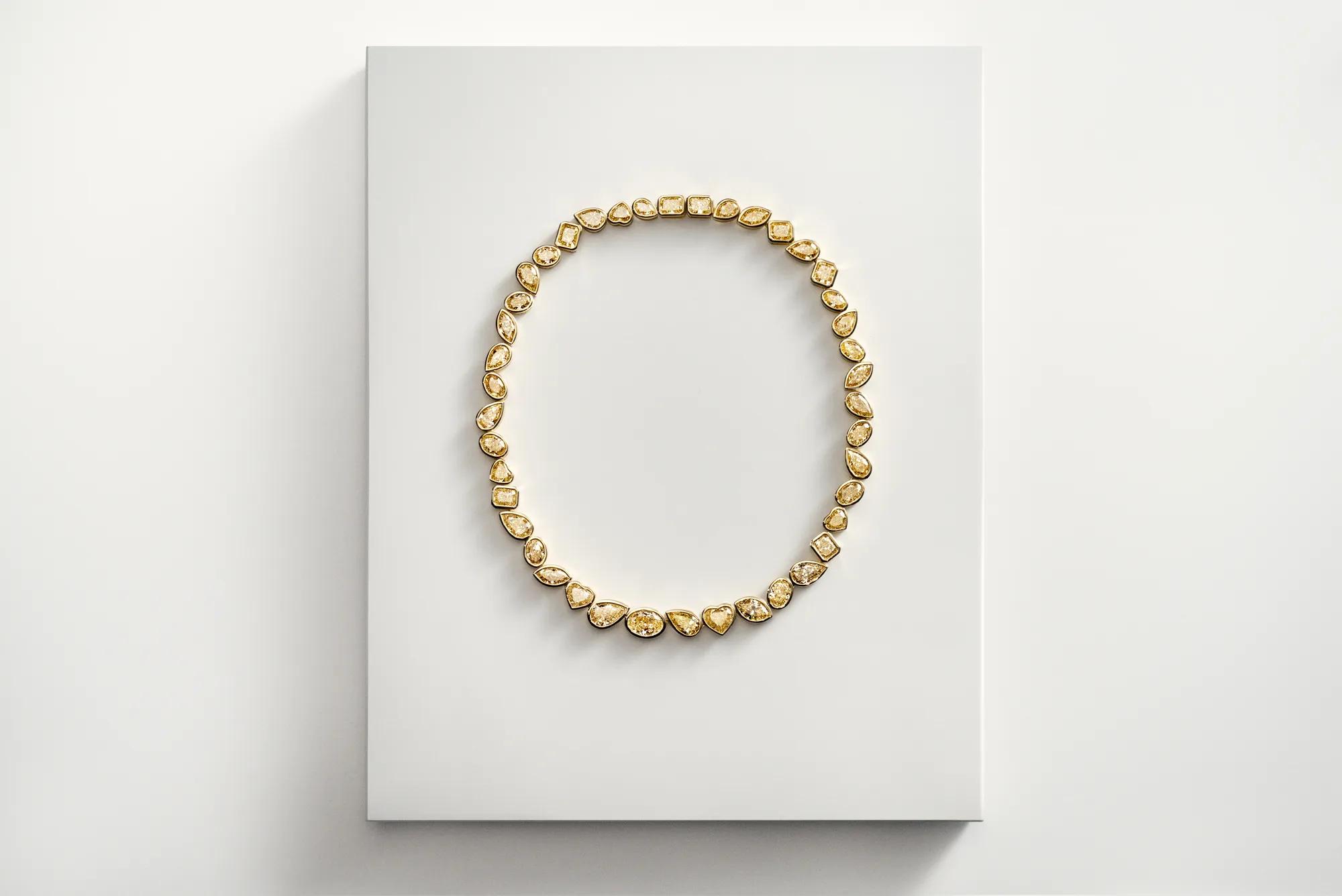 Gold gemstone necklace featuring mixed pear, round, and emerald-cut stones displayed on a white backdrop.