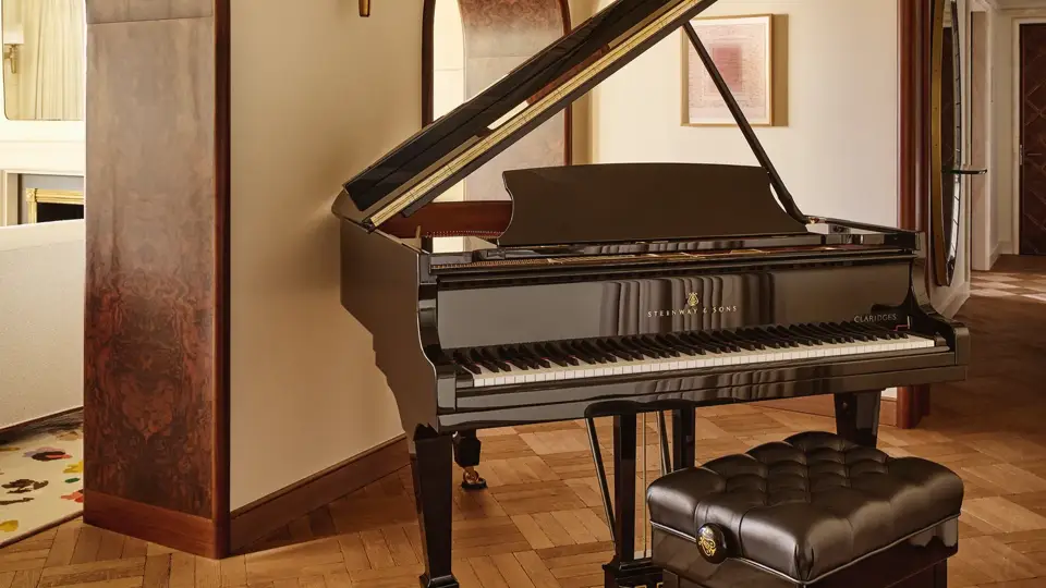 Black grand piano with a padded bench in a warm, elegant room with parquet flooring and arched doorways.