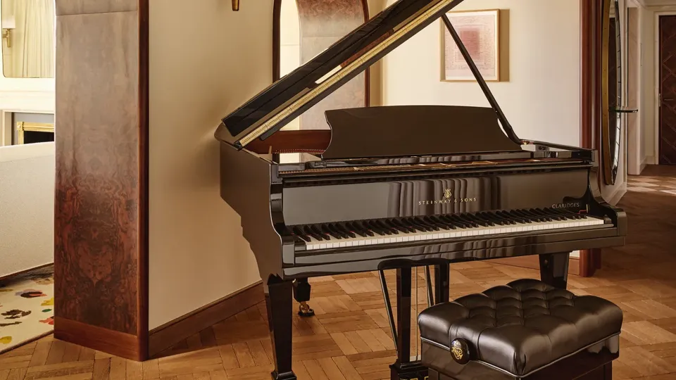 Black grand piano with a padded bench in a warm, elegant room with parquet flooring and arched doorways.