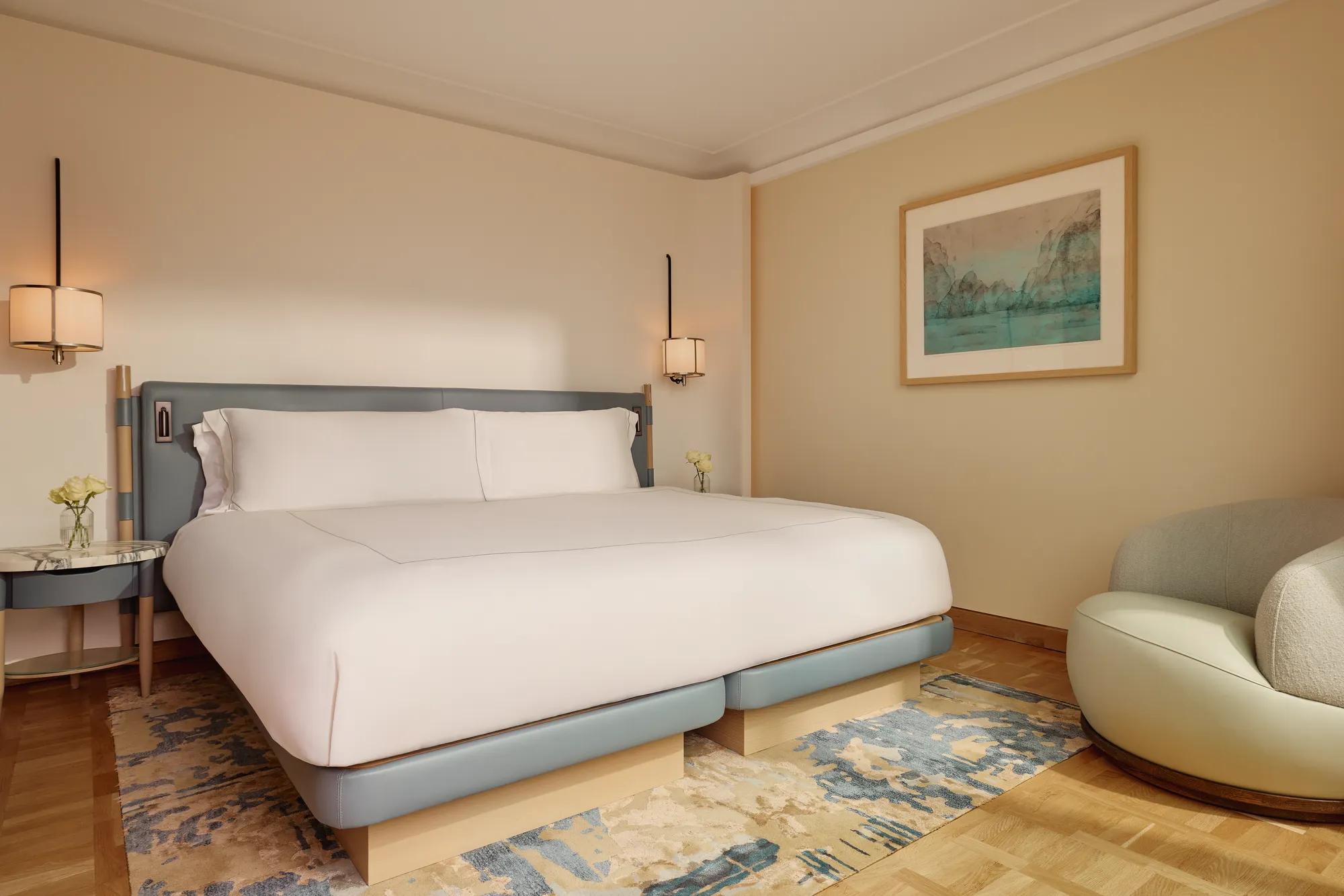 Bedroom with a king-size bed in pale blue and cream tones, bedside tables, and framed landscape artwork on the wall.