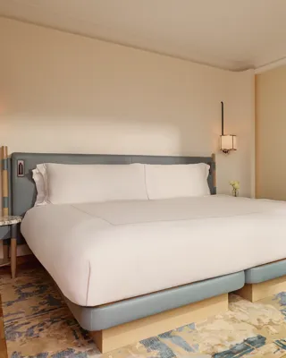 Bedroom with a king-size bed in pale blue and cream tones, bedside tables, and framed landscape artwork on the wall.