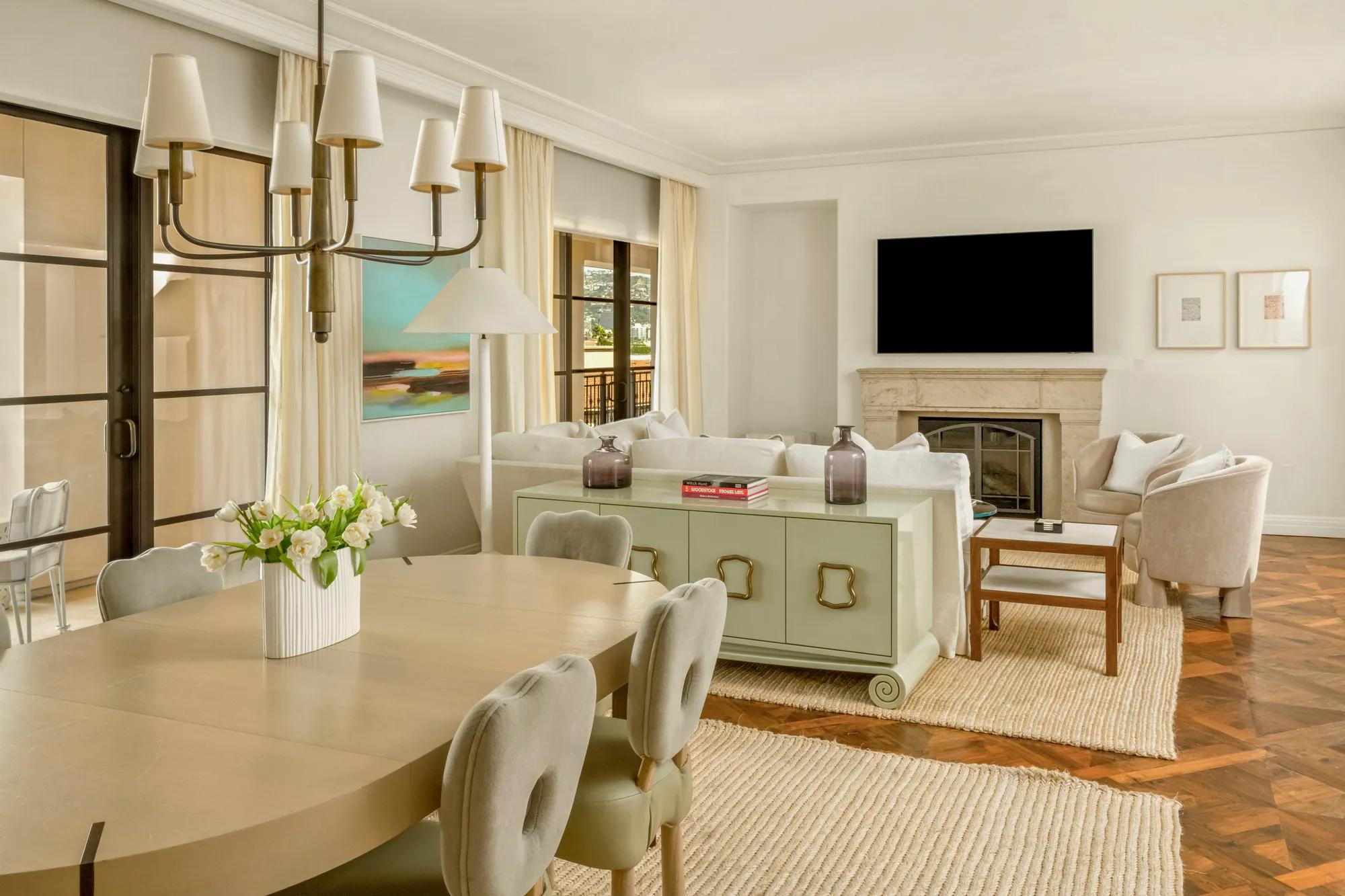 Bright open-plan living and dining area with fireplace, cream furnishings, parquet floors, and large windows with balcony views.