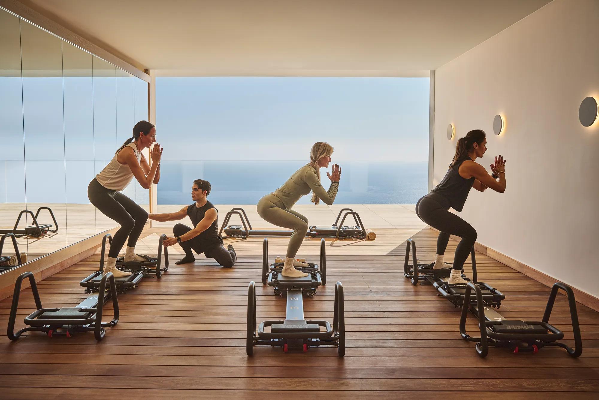 Groupe pratiquant des exercices sur machines de fitness dans un studio lumineux avec vue panoramique sur la mer.