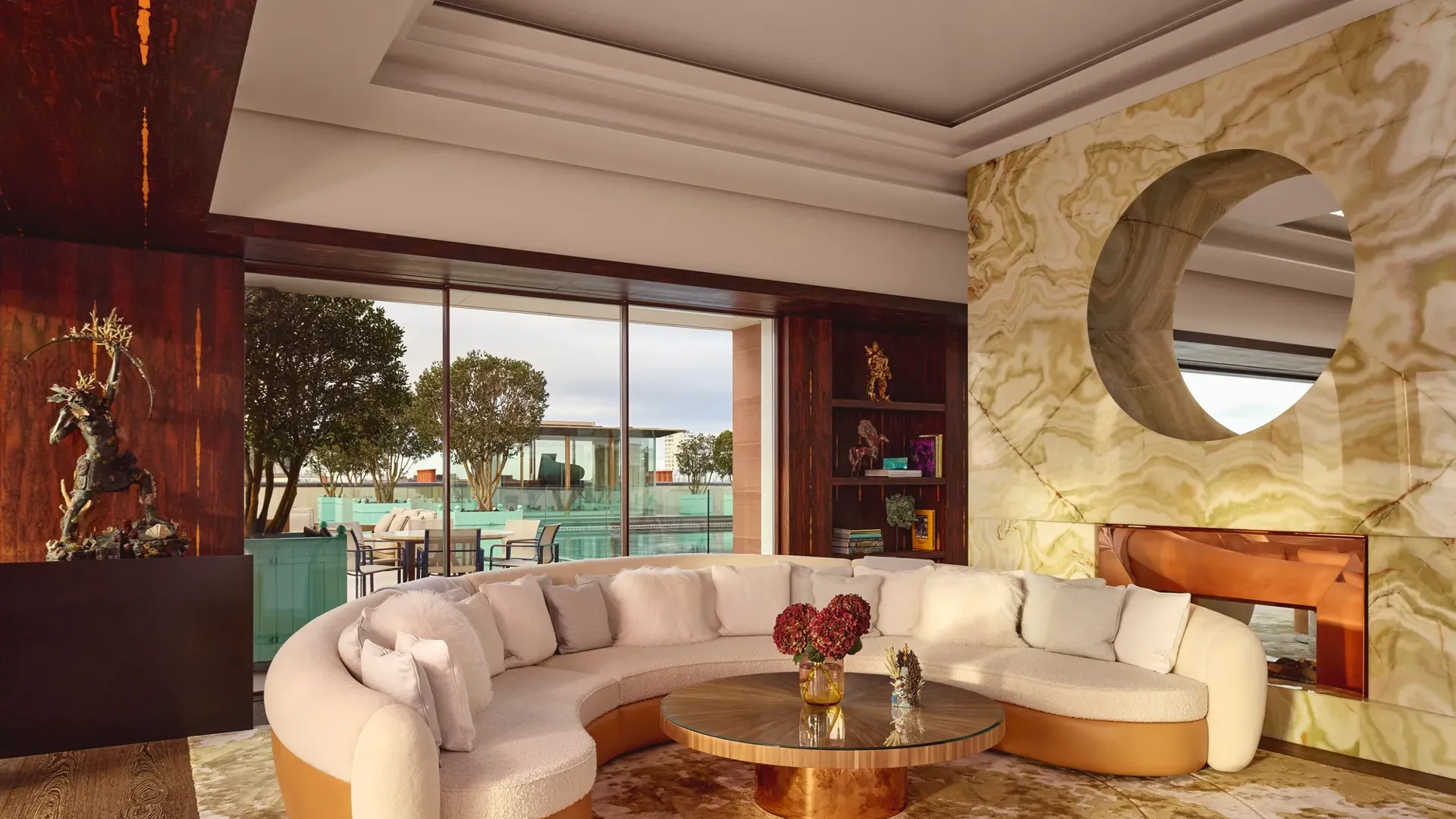 Spacious penthouse living area at Claridge’s with a curved cream sofa, marble fireplace, and glass doors opening to a terrace.