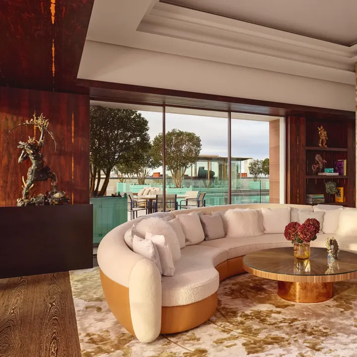Spacious penthouse living area at Claridge’s with a curved cream sofa, marble fireplace, and glass doors opening to a terrace.