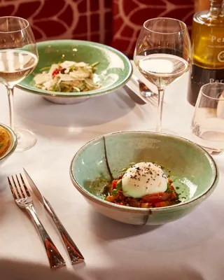 Table with three green ceramic bowls of appetisers, white wine glasses, and olive oil bottle.