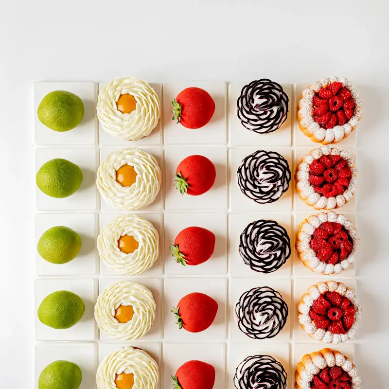 Flat lay of six types of pastries in rows, including lime-shaped, strawberry-shaped, and fruit-topped creations.