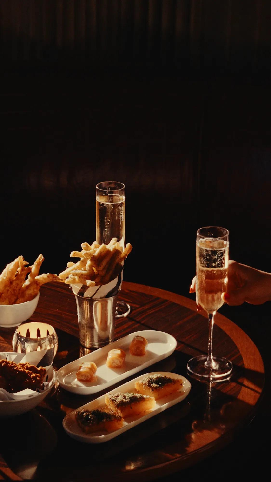 A selection of sparkling wine and elegant bar bites served on a warmly lit table, capturing the intimate atmosphere of a sophisticated cocktail hour.