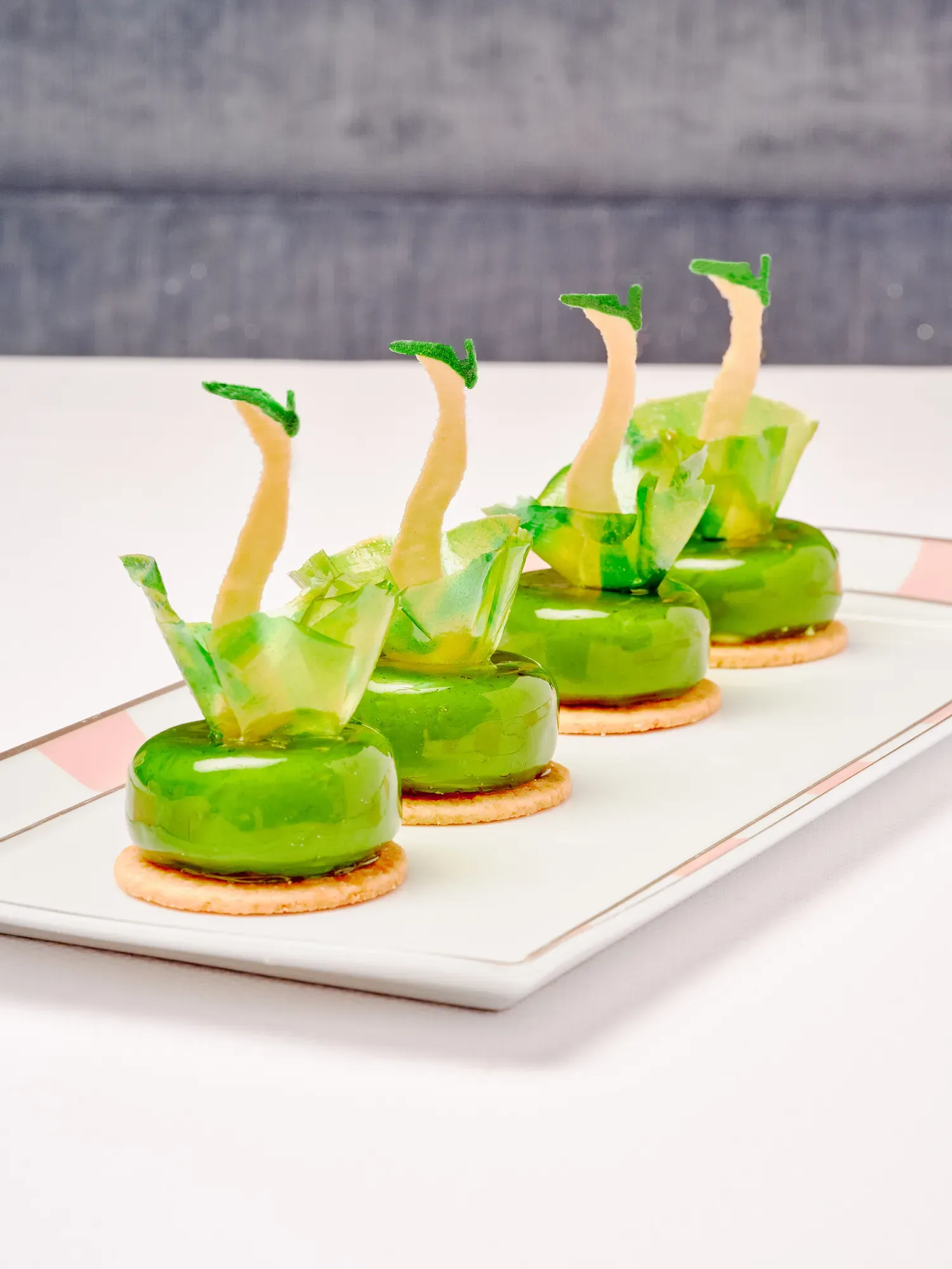 Row of green dress-shaped pastries on biscuits, presented on a rectangular plate.