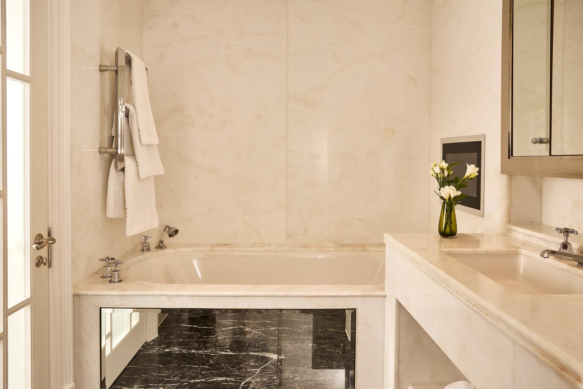 **Alt text:**
Marble bathroom with a soaking bath, vanity, polished dark stone floor and natural light from a tall window.
