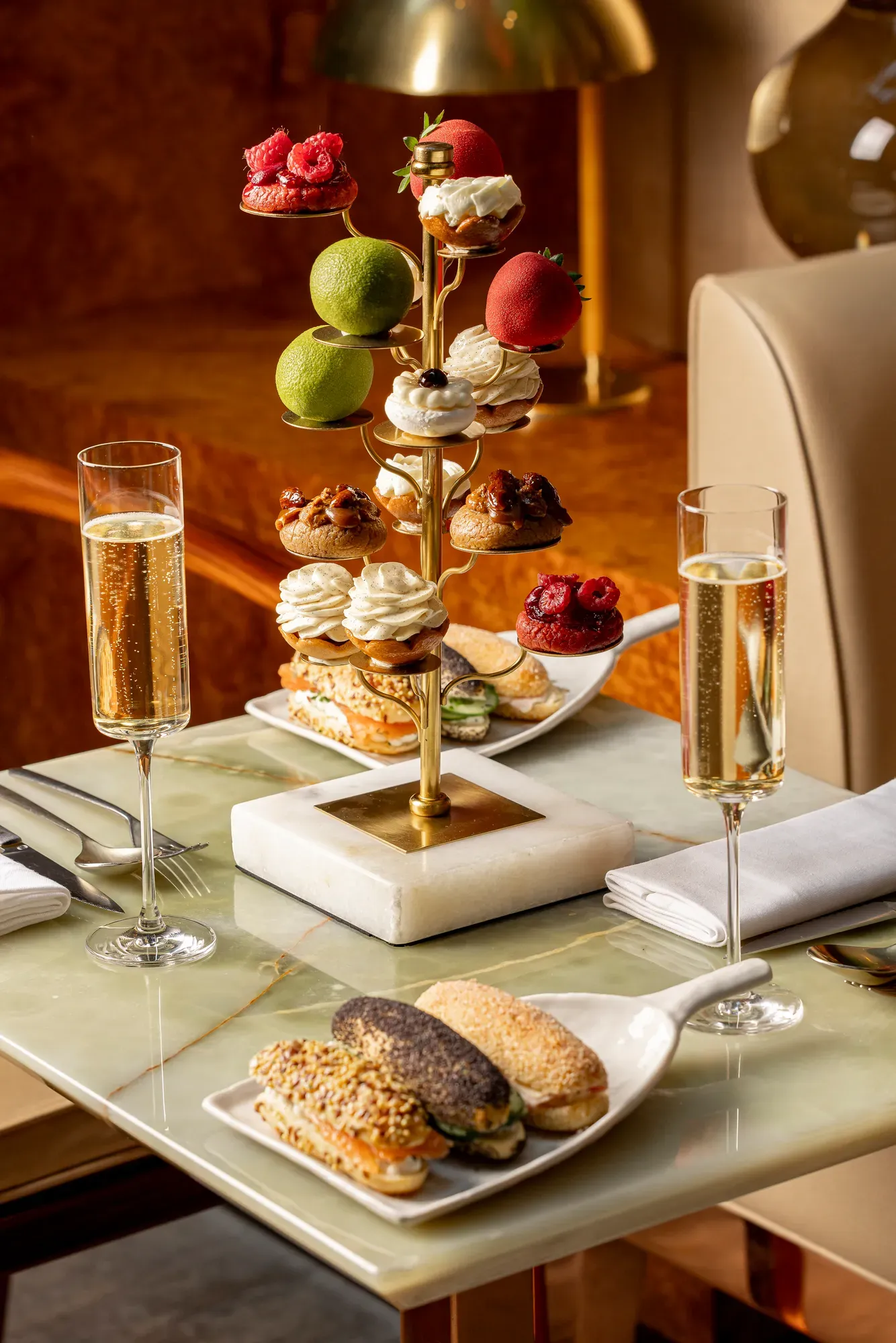 Luxurious afternoon tea with mini pastries and sandwiches served on sculptural stand with champagne flutes.