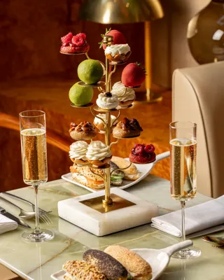 Luxurious afternoon tea with mini pastries and sandwiches served on sculptural stand with champagne flutes.