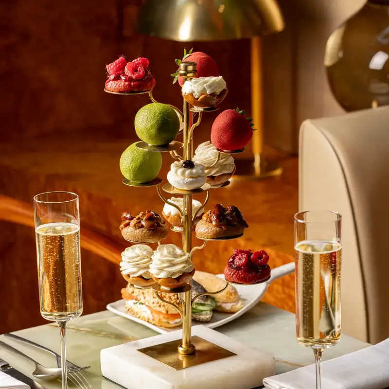 Luxurious afternoon tea with mini pastries and sandwiches served on sculptural stand with champagne flutes.