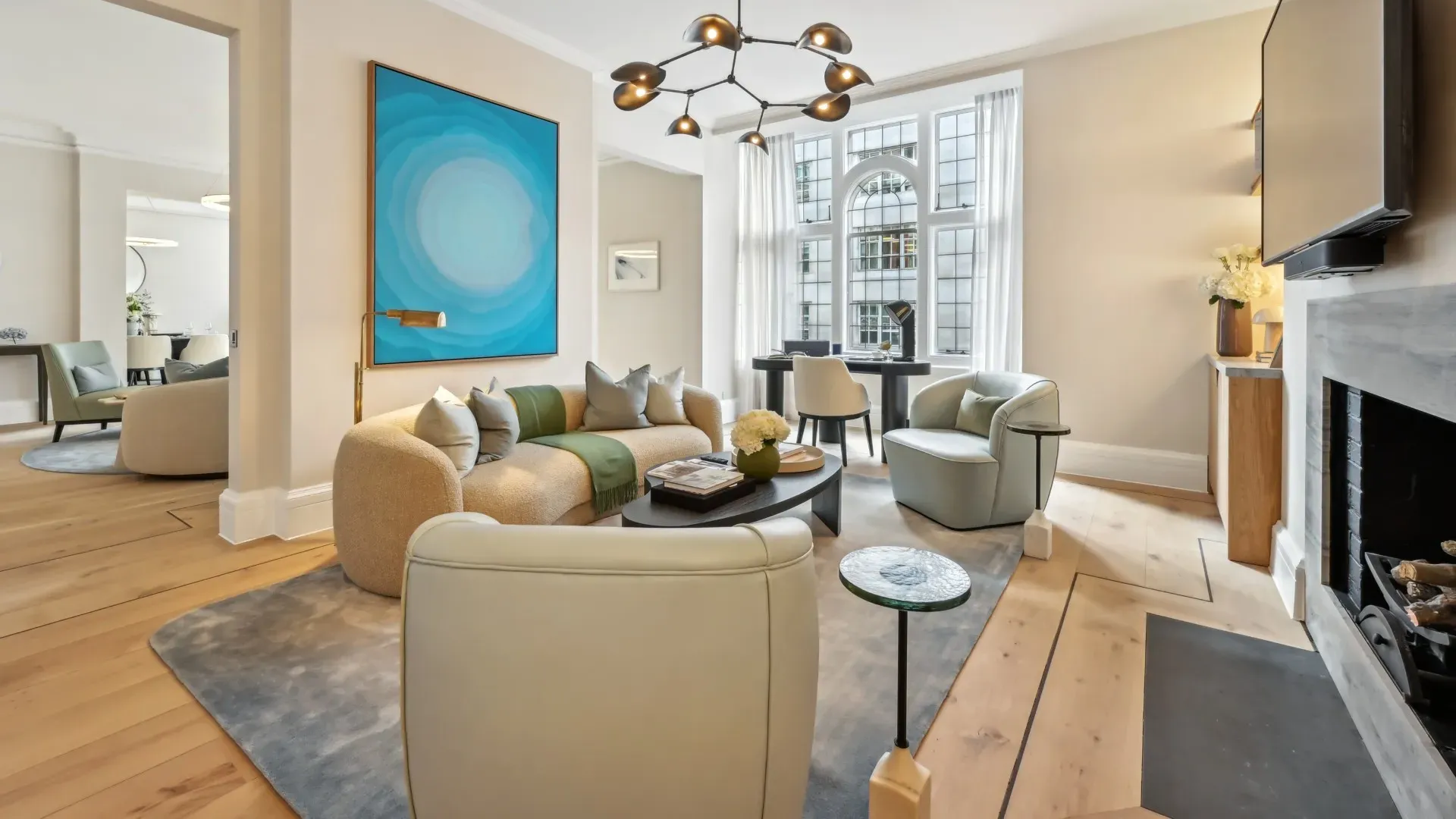 Contemporary living room with curved sofa, bold blue artwork, armchairs, and arched window.