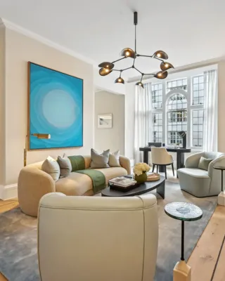 Contemporary living room with curved sofa, bold blue artwork, armchairs, and arched window.