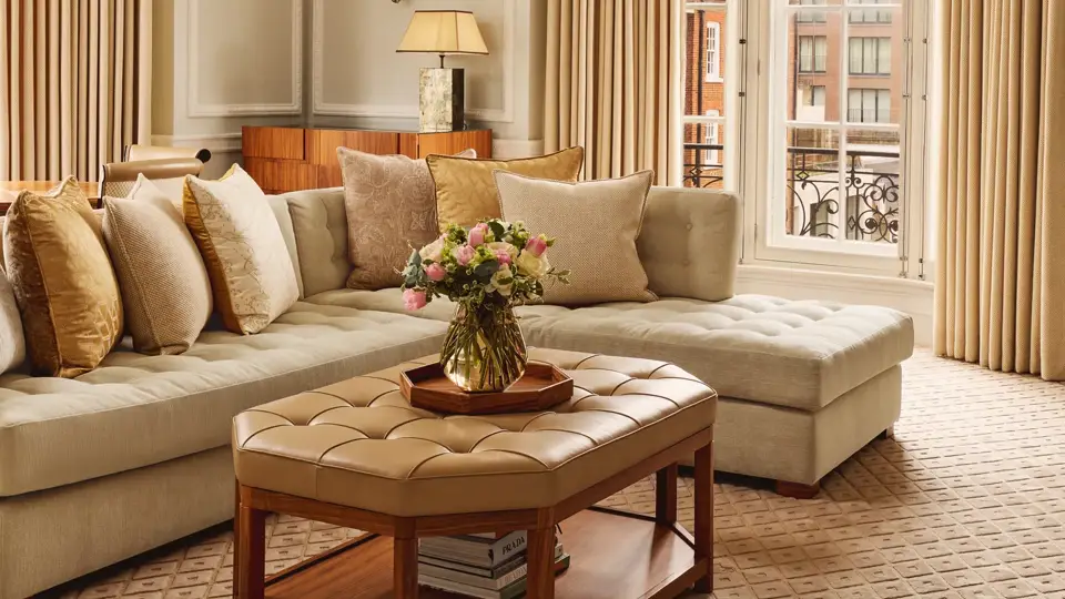 Elegant living room with curved sofa, crystal chandelier, upholstered coffee table, and tall windows overlooking the street.