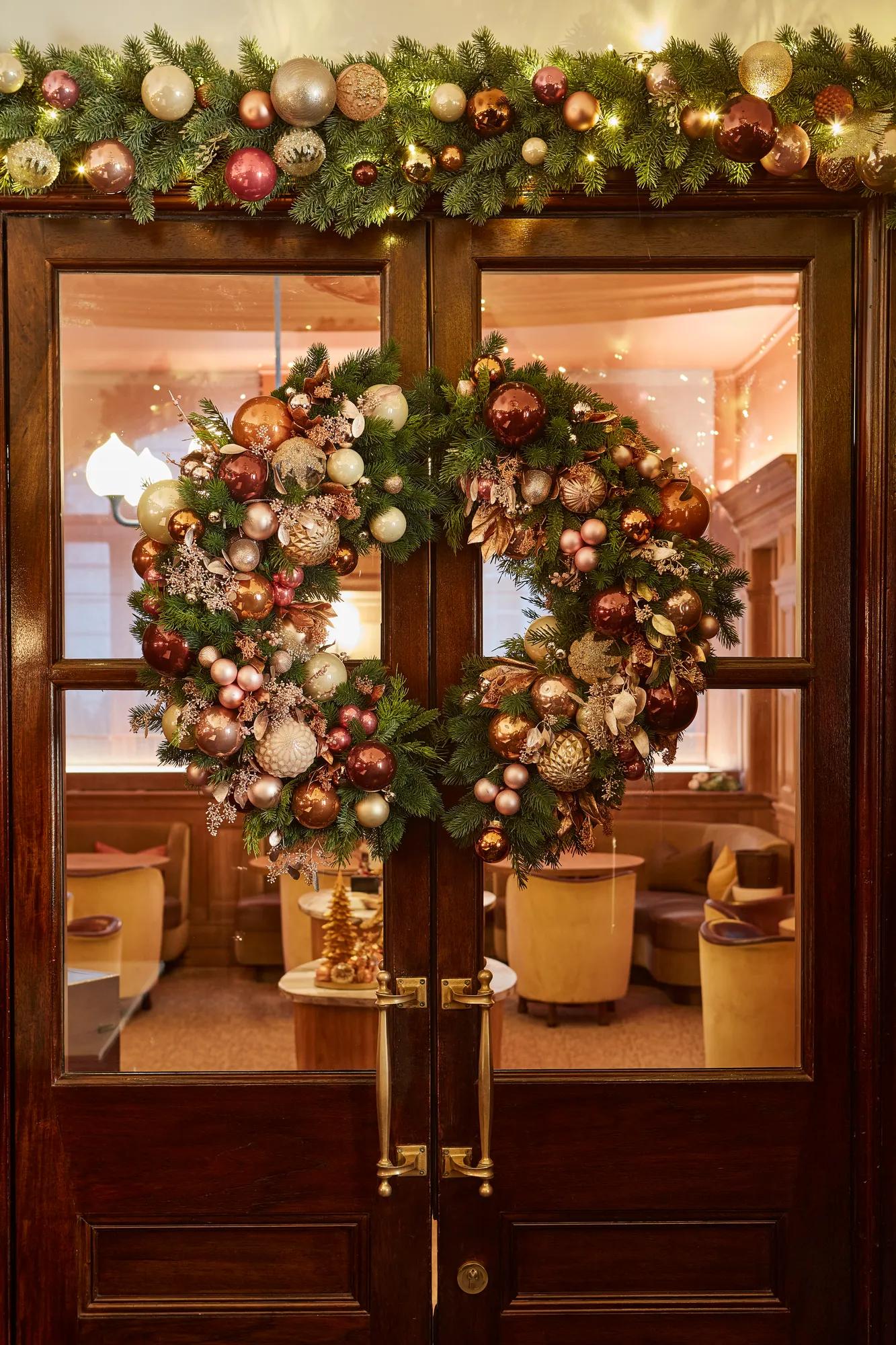 Festive wreaths and garlands decorated with baubles adorn wooden glazed doors.