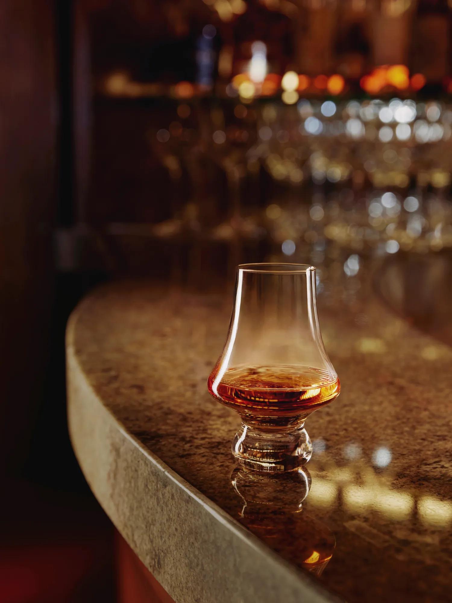 Glencairn glass of whisky on a polished granite bar with warm, out-of-focus bar lights.