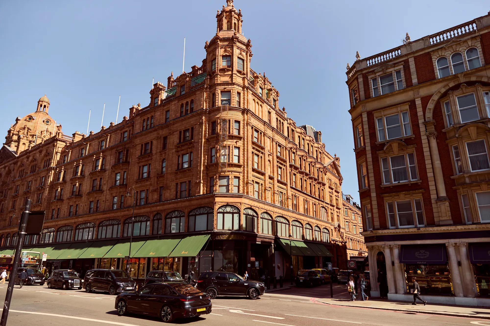 Historic red-brick corner department store on a busy city street, with cars, pedestrians, and clear blue sky.