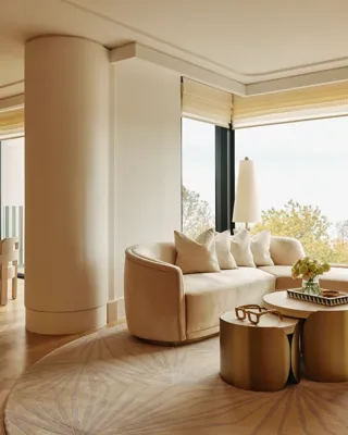Elegant suite with curved cream sofa, gold tables, and dining area, featuring large windows overlooking Hyde Park treetops.